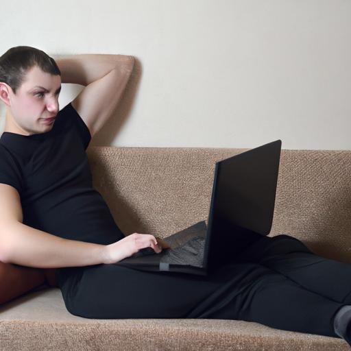 Một chàng trai trẻ mặc áo thun Rush Man nằm trên ghế sofa với laptop